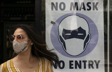 FILE – In this June 23, 2020, file photo, a woman walks out of a liquor store past a sign requesting its customers to wear a mask in Santa Monica, Calif. The number of daily U.S. deaths from the coronavirus is declining again after peaking in early August, but scientists are warning that a new bout with the disease this fall could claim more lives. Experts say the arrival of cooler weather and the likelihood of more indoor gatherings will add to the importance of everyday safety precautions, like wearing masks, staying home and washing hands. (AP Photo/Jae C. Hong, File) NYAG701 NYAG701