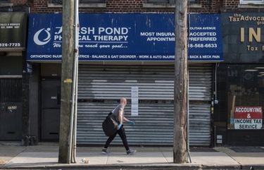 A pedestrian wearing protective gloves passes in front of a physical therapy closed on Metropolitan Avenue in the Queens borough of New York, U.S., on Tuesday, April 7, 2020. Anthony Fauci, director of the U.S. National Institute of Allergy and Infectious Diseases, said the start of a turnaround in the fight against the virus could come after this week. Photographer: Christopher Occhicone/Bloomberg 775503306
