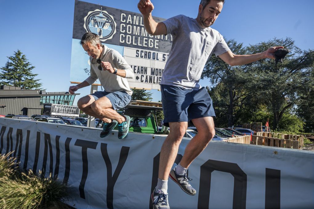 Back in college again Mark, left, and Brian Canlis jump down after working on the Canlis Community College billboard. (Steve Ringman / The Seattle Times)