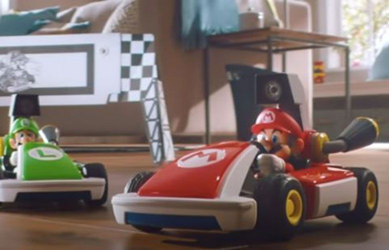 Nintendo video screenshot .  New Nintendo augmented reality title, “Mario Kart Live: Home Circuit,” the Switch controls a small, physical remote control kart with a camera. Players set a course by drawing the route and setting up small gates throughout the play area. 