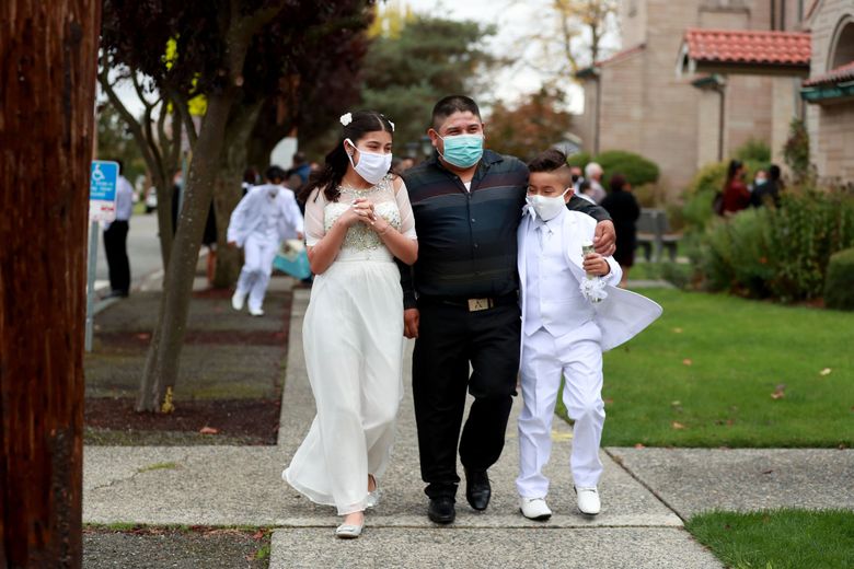 Leslie Nuñez, 12, left; her uncle Juan Nuñez;  and brother Brandon Nuñez, 9, leave First Communion at Holy Family Roman Catholic Church in White Center. Juan, the kids’ godfather, says their First Communion was scheduled for spring  but delayed until October. The service was held with safety precautions, including temperature checks, hand-sanitizing stations and social distancing. “It was nice to the see the families,” Juan says. “I was happy to go back inside the church.” (Erika Schultz / The Seattle Times)