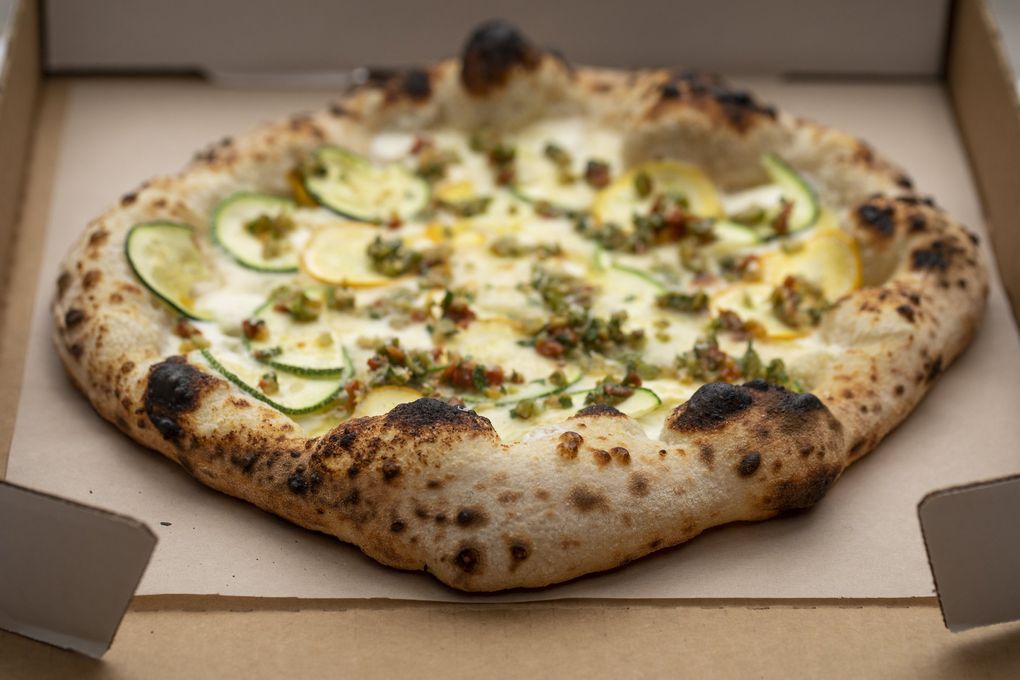 Tiny Industries’ summer squash pizza comes adorned with ricotta, provolone, mozzarella and squash and is finished with a relish of sun-dried tomatoes, olives and preserved lemons. The blistered crust is naturally leavened dough cooked in a portable, high-temperature oven.
(Bettina Hansen / The Seattle Times)