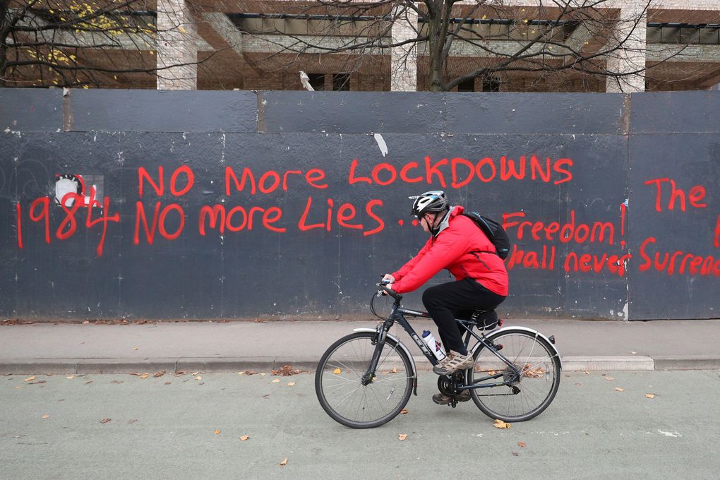 A man cycles past anti-lockdown graffiti in Manchester, England, Monday, Oct. 19, 2020 as the row over Greater Manchester region’s coronavirus status continues. Britain’s government says discussions about implementing stricter restrictions in Greater Manchester must be completed Monday because the public health threat caused by rising COVID-19 infections is serious and getting worse. (Peter Byrne/PA via AP)
