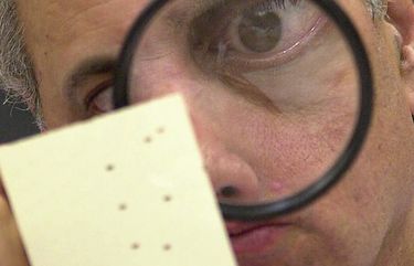 FILE – This Nov. 24, 2000 file photo shows Broward County canvassing board member Judge Robert Rosenberg using a magnifying glass to examine a disputed ballot at the Broward County Courthouse in Fort Lauderdale, Fla. Twenty years ago, in a different time and under far different circumstances than today, it took five weeks of Florida recounts and court battles before Republican George W. Bush prevailed over Democrat Al Gore by 537 votes.  (AP Photo/Alan Diaz, File) WX101 WX101