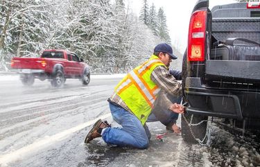 Jacob Morrelli works in the snow and sleet to get chains on his truck about 8 miles from the summit at Stevens Pass on Friday November 13th, 2020. Chains were required for driving over the pass on Friday. There is a winter storm warning from Skykomish to the pass along Highway 2 this weekend.  215653