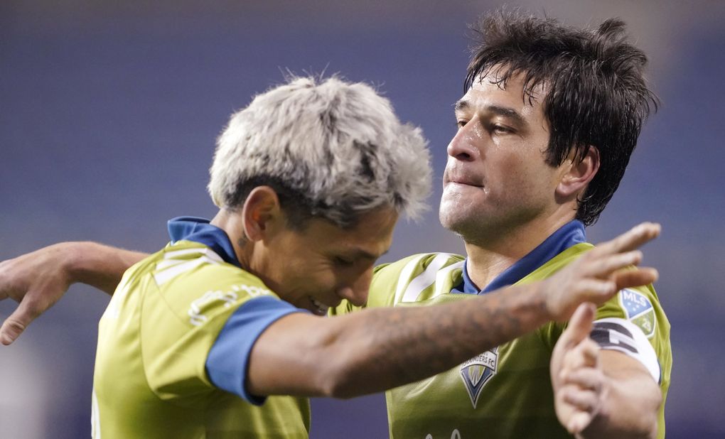 Seattle Sounders’ Raul Ruidiaz, left, and Nicolas Lodeiro embrace after the team’s 1-0 win over FC Dallas in an MLS playoff soccer match Tuesday, Dec. 1, 2020, in Seattle. (Ted S. Warren / The Associated Press)