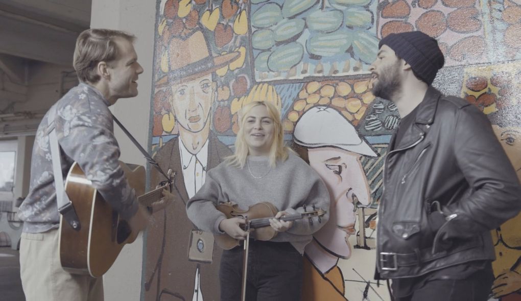 In a new concert film, The Head and the Heart’s Jonathan Russell (from right) and Charity Rose Thielen reunite with former bandmate Josiah Johnson at their old Pike Place Market busking spot. (Carlos Cruz)