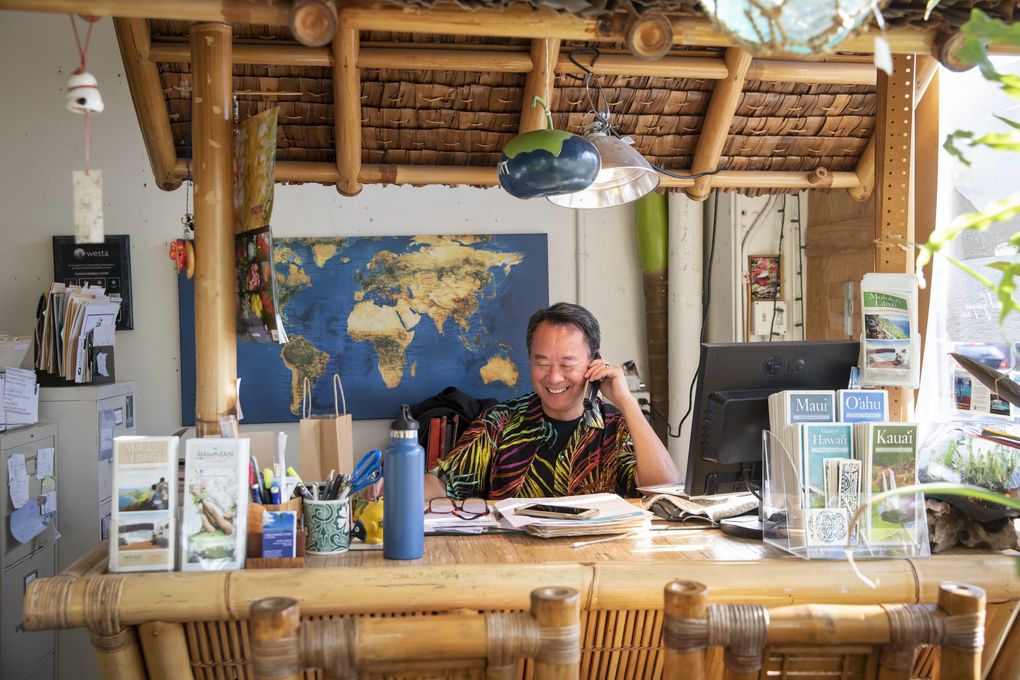 Terry Uemura, travel consultant and manager, talks on the phone with a client at his tiki-themed desk at Hawaii General Store and HGS Travel in Seattle’s Wallingford neighborhood Jan. 22, 2021. (Bettina Hansen / The Seattle Times)
