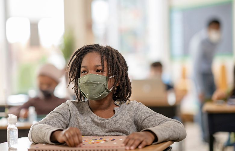 School girl sitting at desk working on a STEM project while wearing a protective face mask due to new COVID-19 regulations