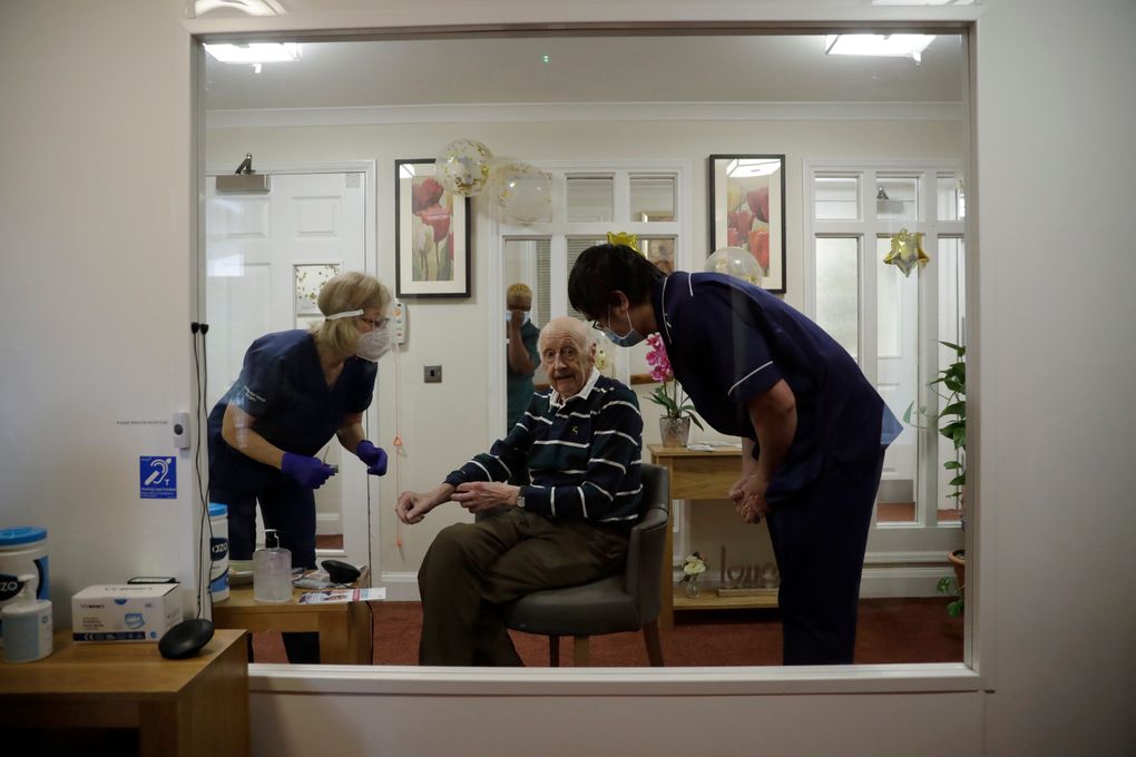 Care home resident John Peake, aged 96 and an Olympic silver medalist for the British field hockey team at the London 1948 Summer Olympics, is seen through a viewing screen installed for residents to safely receive visits from family members during the coronavirus outbreak, as he prepares to roll up his sleeve to receive his first dose of the Oxford/AstraZeneca COVID-19 vaccine from Dr. Jane Allen at the Wimbledon Beaumont Care Home, run by Barchester, in south west London, Wednesday, Jan. 13, 2021, during England’s third national lockdown since the coronavirus outbreak began. (AP Photo/Matt Dunham)