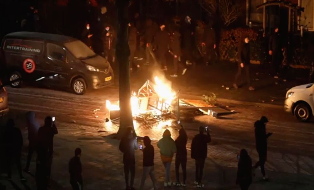 In this grab taken from video on Monday, Jan, 25, 2021, people use their phones to film items burning on a fire started by rioters, in Haarlem, Netherlands. Groups of youths confronted police in several Dutch cities defying the country’s coronavirus curfew and throwing fireworks. (Mizzle Media via AP)