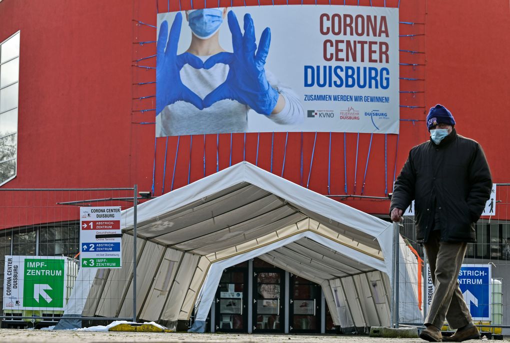 A man with a face mask walks past the Corona Center in Duisburg, Germany, Monday, Jan. 25, 2021. The former Musical theater has been turned into a COVID-19 test and vaccination center. Vaccinations outside care homes and hospitals are delayed. (AP Photo/Martin Meissner)