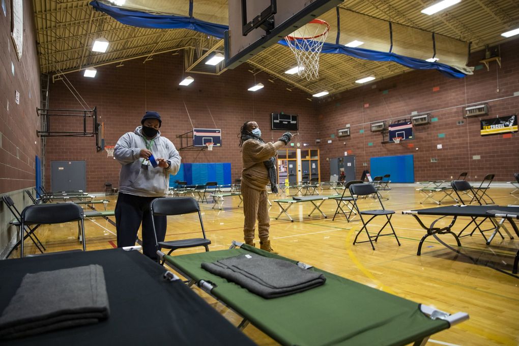 Recreation leaders George Yasutake, left, and Traci Grant of the Seattle Parks and Recreation finish setting up 41 beds in the gymnasium at the Garfield Community Center as an emergency winter shelter Thursday. Fisher Pavilion at the Seattle Center is also open as an emergency cold-weather shelter, as well as the Jefferson Day Center, which is for men only. (Bettina Hansen / The Seattle Times)