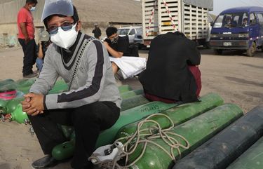 Catholic priest Diego German sits on empty oxygen cylinders as he waits to refill his tank for his father who is suffering from COVID-19, in the Villa El Salvador neighborhood of Lima, Thursday morning, Feb. 18, 2021, as the lack of medical oxygen to treat new coronavirus patients continues to be the norm in Peru. Long lines form outside private providers with many spending the night outside so as to not lose their place in line. (AP Photo/Martin Mejia) LIM105 LIM105