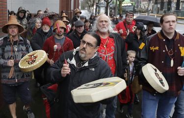 FILE – In this Jan. 6, 2020, file photo, Tony A. (Naschio) Johnson, center, elected chairman of the Chinook Indian Nation, plays a drum as he leads tribal members and supporters as they march to the federal courthouse in Tacoma, Wash., as they continue their efforts to regain federal recognition. As COVID-19 disproportionately affects Native American communities, many tribal leaders say the pandemic poses particular risks to tribes without federal recognition. The Chinook Nation received some federal funding through a local nonprofit for small tribes to distribute food to elders and help with electricity bills, tribal Johnson said. (AP Photo/Ted S. Warren, File) WATW402 WATW402