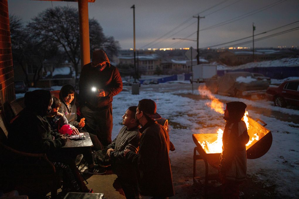 The Traugott family, with no power in their apartment, play a game of Uno outside while warming up near burning wood scavenged from a discarded armoire in Austin, Texas, Feb. 17, 2021. (Tamir Kalifa / The New York Times)