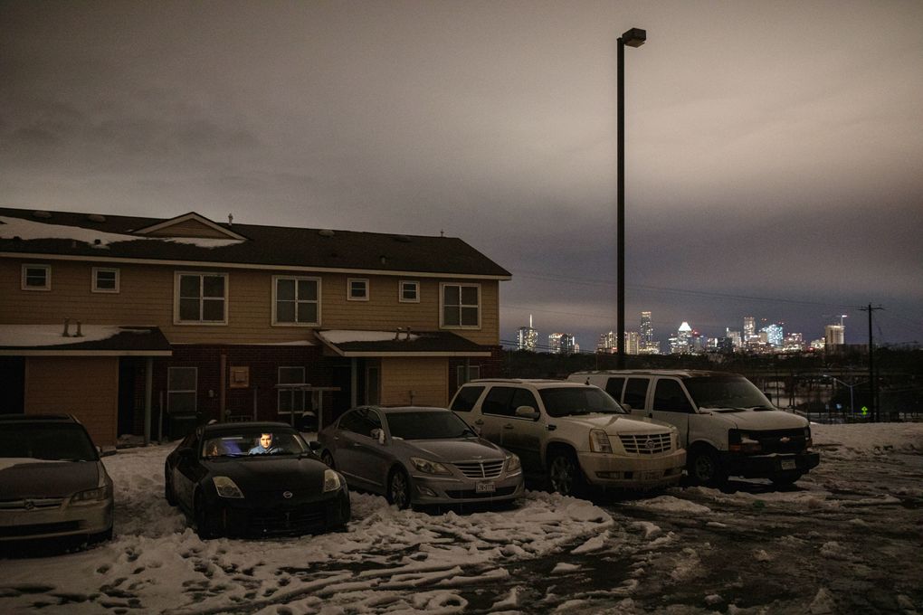 Two people warm up and charge a cellphone by running their parked car outside residences without electricity, not far from downtown Austin, Texas, Feb. 16, 2021. (Tamir Kalifa / The New York Times)