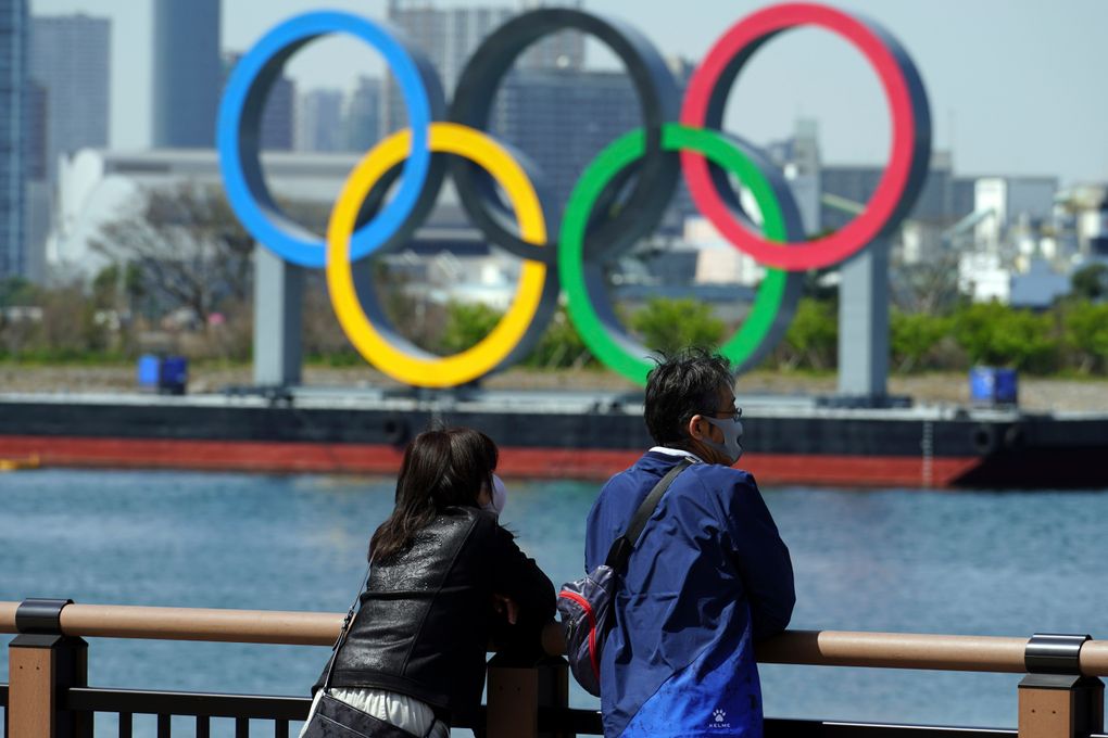 A man and a woman stand with a backdrop of the Olympic rings floating in the water in the Odaiba section Thursday in Tokyo. (AP Photo/Eugene Hoshiko)