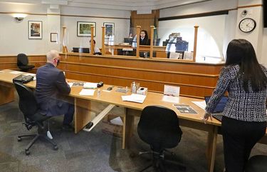 A plexiglass shield stands between King County Superior Court Chief Criminal Judge Patrick Oishi, in the background facing camera, and from left in the foreground, all socially distanced: a podium for a criminal defendant; his public defender Carey Huffman; and senior deputy prosecutor TinaMarie Masters, during a motion to remand criminal hearing Wednesday, May 6, 2020 in Seattle. The shield and room reconfiguration is part of modifications made during the coronavirus outbreak in one of the busiest courtrooms in the city.