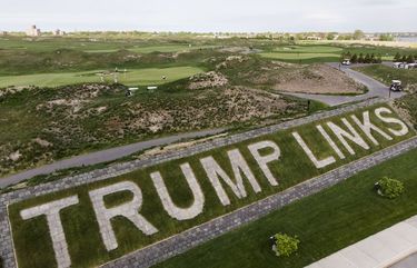Patrons play the links as a giant branding sign is displayed with flagstones at Trump Golf Links at Ferry Point in the Bronx borough of New York on Tuesday, May 4, 2021. Former President Donald Trump has a rich history of fighting back when he’s down and making others pay, and that’s exactly how he intends to deal with New York City over its plans to fire his company from running the city golf course. (AP Photo/John Minchillo) NYJM504 NYJM504