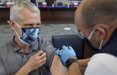 Paul Clasby, of Holliston, Mass., left, receives his second shot of Moderna COVID-19 vaccine from paramedic Jake Lees, of North Attleborough, Mass., right, at a mass vaccination clinic, Wednesday, May 19, 2021, at Gillette Stadium, in Foxborough, Mass. A month after every adult in the U.S. became eligible for the vaccine, a distinct geographic pattern has emerged: The highest vaccination rates are concentrated in the Northeast, while the lowest ones are mostly in the South. (AP Photo/Steven Senne) NYAG506 NYAG506