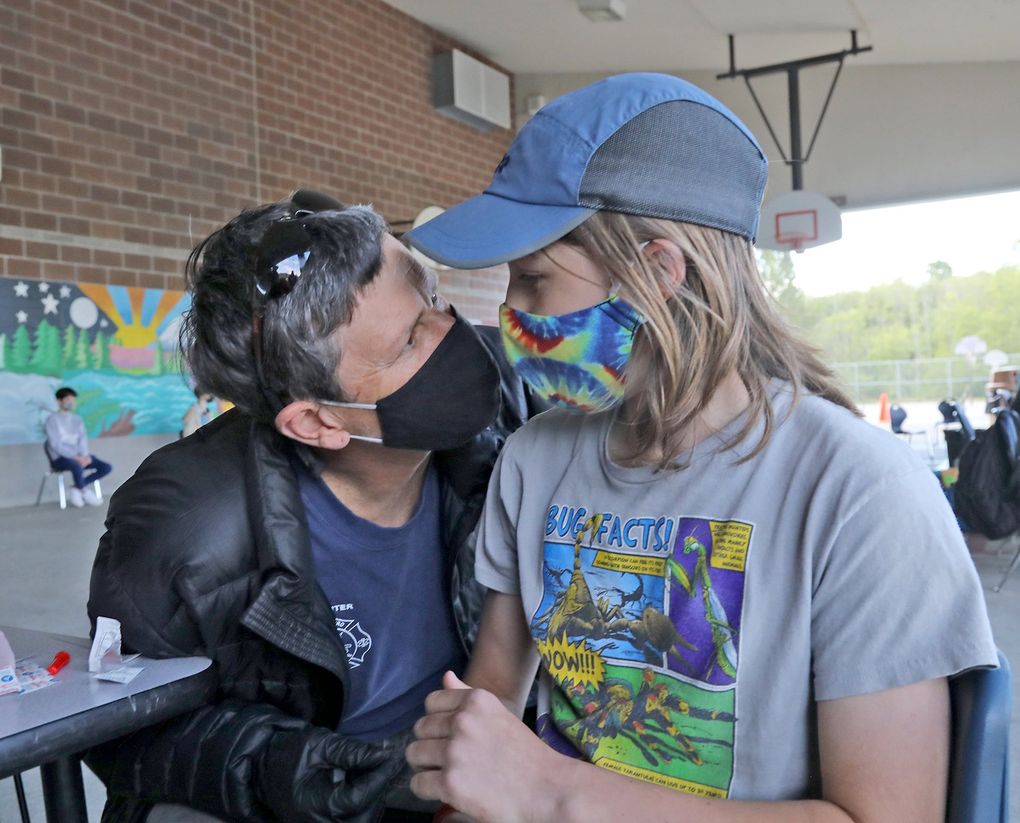 Seattle Fire Department Lt. Penny Stone hugs her son, Calder Stone, 12, after giving him the Pfizer vaccine Thursday at Pathfinder K-8 in West Seattle. Vaccinators at the school pop-up clinic were all Seattle Fire Department employees. (Greg Gilbert / The Seattle Times)