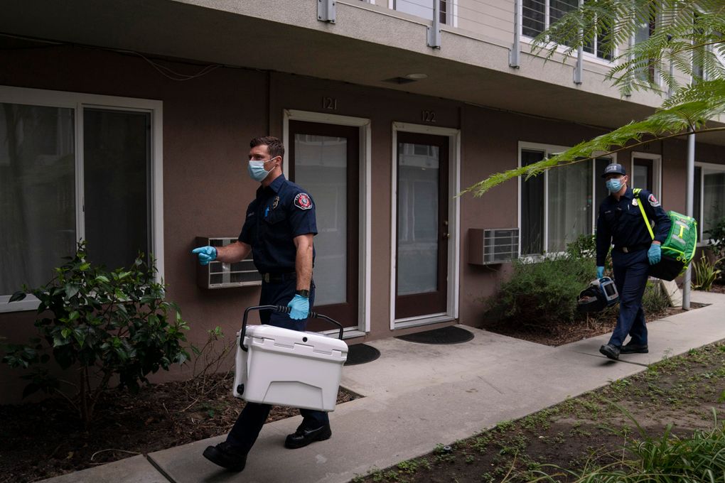 Torrance firefighter Trevor Borello, left, carries a cooler containing the Pfizer COVID-19 vaccine as he walks to an apartment to inoculate two sisters suffering from muscular dystrophy, Wednesday, May 12, 2021, in Torrance, Calif. Teamed up with the Torrance Fire Department, Torrance Memorial Medical Center started inoculating people at home in March, identifying people through a city hotline, county health department, senior centers and doctor’s offices, said Mei Tsai, the pharmacist who coordinates the program. (AP Photo/Jae C. Hong)