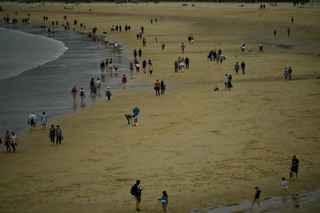 People walk along La Concha beach, after lockdown restrictions were lifted, in San Sebastian, northern Spain, Sunday, May 9, 2021. Impromptu street celebrations erupted across Spain as the clock struck midnight on Saturday, when a six-month-long national state of emergency to contain the spread of coronavirus ended and many nighttime curfews were lifted. (AP Photo/Alvaro Barrientos)