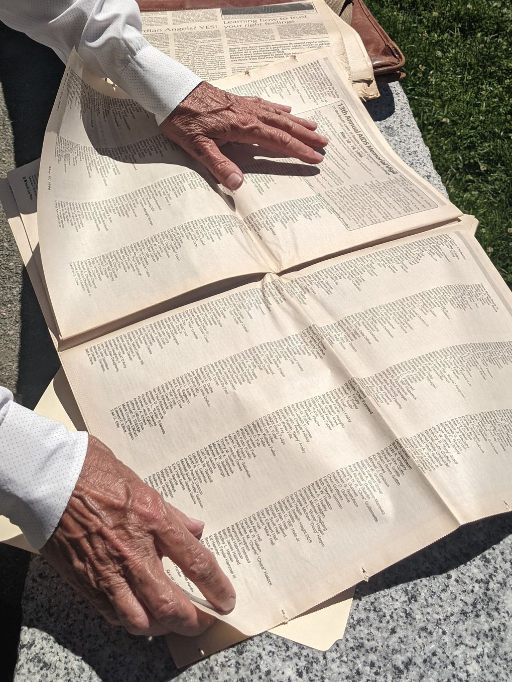 Former Seattle City Councilmember Tom Rasmussen shares a 1996 issue of Seattle Gay News that lists the names of community members who lost their lives to AIDS. (Crystal Paul / The Seattle Times)