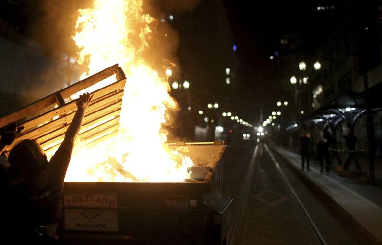 Protesters light a fire in a dumpster in downtown Portland, Ore., Friday, April 16, 2021. Police in Portland, said Saturday they arrested several people after declaring a riot Friday night when protesters smashed windows, burglarized businesses and set multiple fires during demonstrations that started after police fatally shot a man while responding to reports of a person with a gun. (Dave Killen/The Oregonian via AP) ORPOR501 ORPOR501