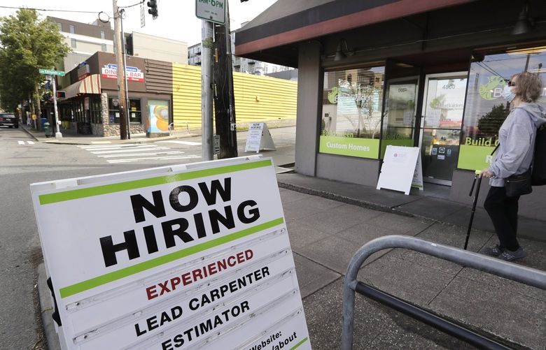 FILE – In this June 4, 2020 file photo, a pedestrian wearing a mask walks past a reader board advertising a job opening for a remodeling company, in Seattle.  (AP Photo/Elaine Thompson, File)