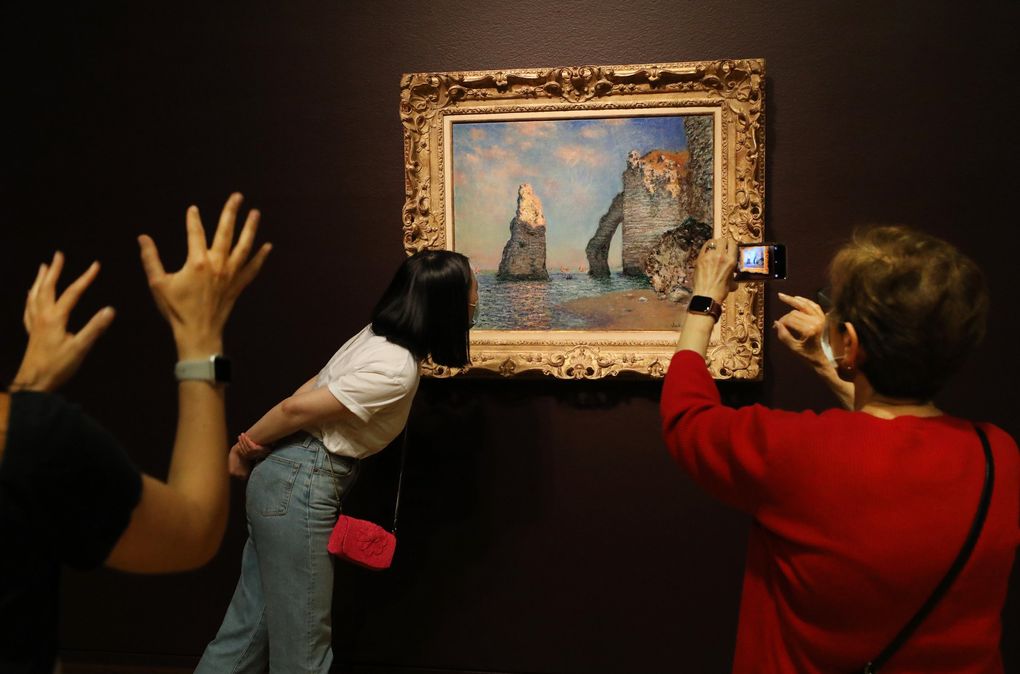 Claude Monet’s “The Cliffs at Étretat,” an 1885 oil on canvas, draws close scrutiny, a reaction and a photograph at SAM’s members preview on June 25. “Monet at Étretat” opens to the public July 1. (Alan Berner / The Seattle Times)
