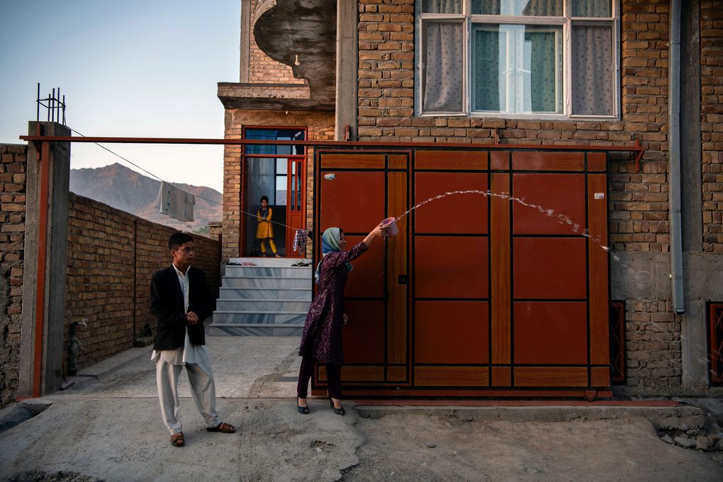The sister and brother of Afghan Air Force Maj. Naiem Asadi throw water behind the family as they leave their house in Kabul — a tradition that is supposed to bring light to the path of a traveler and bring them home sooner — on June 1, 2021. (Kiana Hayeri / The New York Times)