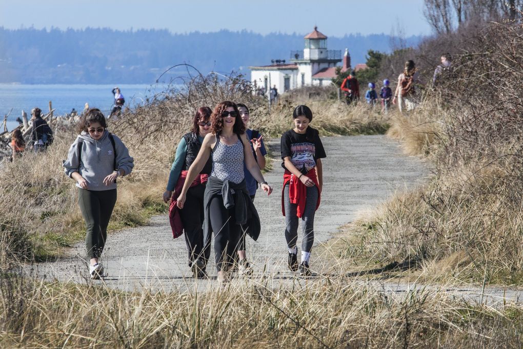 Walkers on the South Beach Trail at Discovery Park, with the West Point Lighthouse in the background, enjoy the unusual sunshine in March 2020. (Steve Ringman / The Seattle Times)