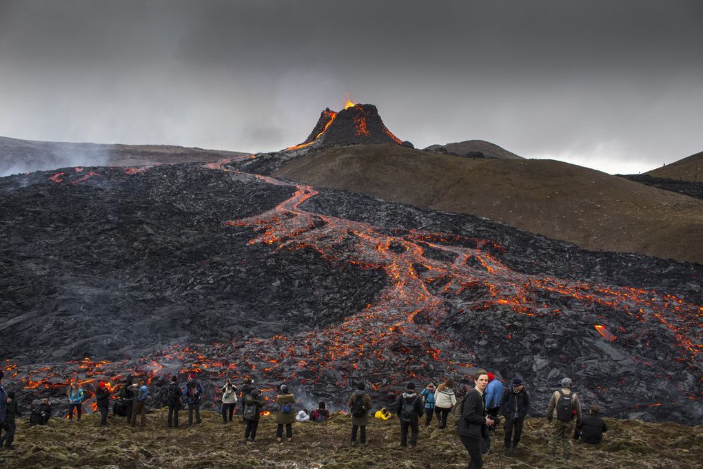 People watch and take photos as lava flows from an eruption of a volcano on the Reykjanes Peninsula in southwestern Iceland March 23, 2021. Nonstop flights to Reykjavík are available out of Seattle-Tacoma International Airport and Iceland is open to visitors. (Marco Di Marco / The Associated Press)