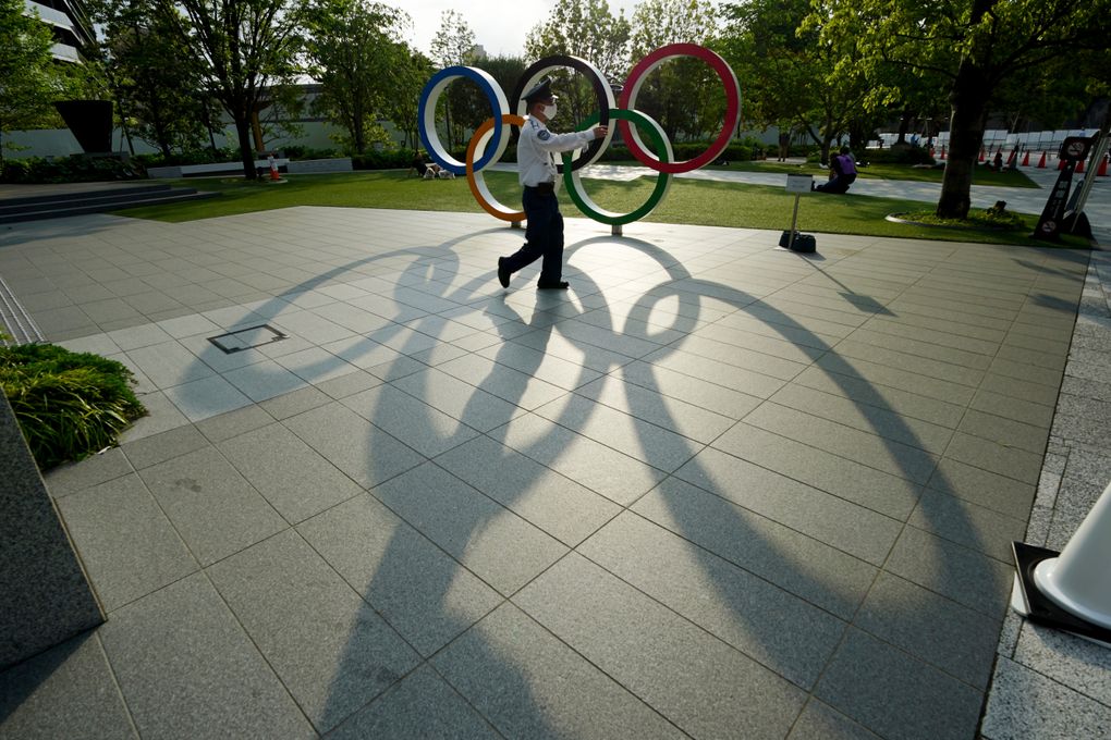 FILE – In this May 9, 2021, file photo, a security guard wearing a protective mask to help curb the spread of the coronavirus walks in front of the Olympic Rings, in Tokyo. Japan, seriously behind in coronavirus vaccination efforts, is scrambling to boost daily shots as the start of the Olympics in July closes in. (AP Photo/Eugene Hoshiko, File)