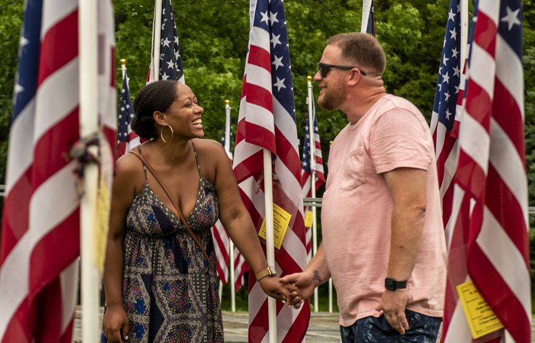 Maryneily Rodriguez, left, and her fiance, Anthony Dipolito, walk through American flags placed in memory of veterans in Greenport, N.Y., July 1, 2021. In a Long Island town, neighbors now make assumptions, true and sometimes false, about people who conspicuously display American flags. (Johnny Milano/The New York Times)
