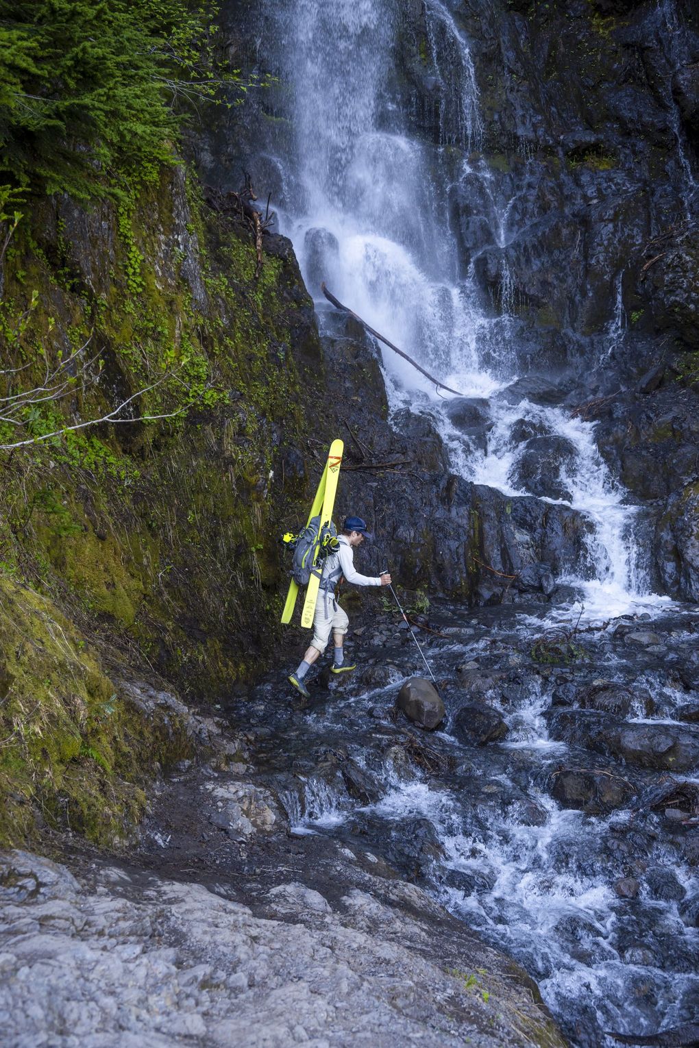 Trevor Kostanich crosses below a cascading waterfall on the Heliotrope Ridge trail during the exit from Mount Baker. Each peak required significant mileage of trail walking before skis could be employed on the glaciers and seasonal snow fields. (Scott Rinckenberger)