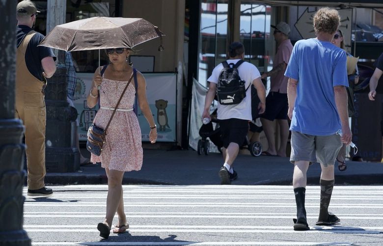 A person uses an umbrella for shade from the sun while walking near Pike Place Market, Tuesday, June 29, 2021, in Seattle. The unprecedented Northwest U.S. heat wave that slammed Seattle and Portland, Oregon, moved inland Tuesday â€” prompting an electrical utility in Spokane, Washington, to resume rolling blackouts amid heavy power demand.  (AP Photo/Ted S. Warren)