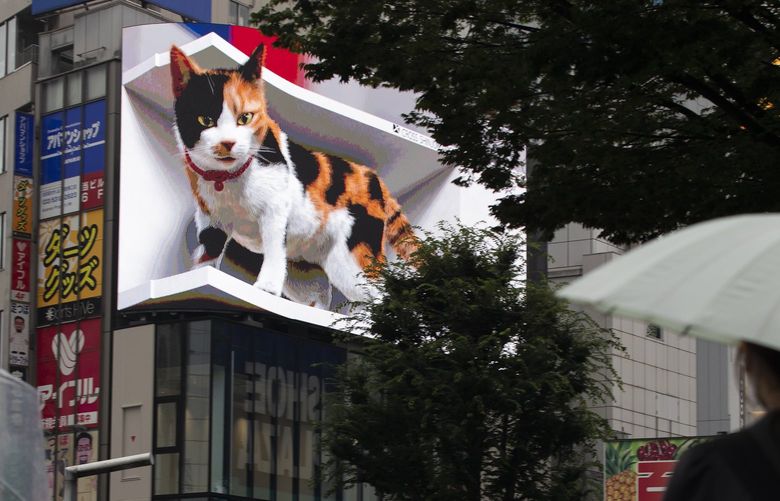People walk by a 3D video advertisement display of a giant cat that was recently installed in the famed Shinjuku shopping district in Tokyo on Friday, July 9, 2021. (AP Photo/Hiro Komae) TKHK501 TKHK501