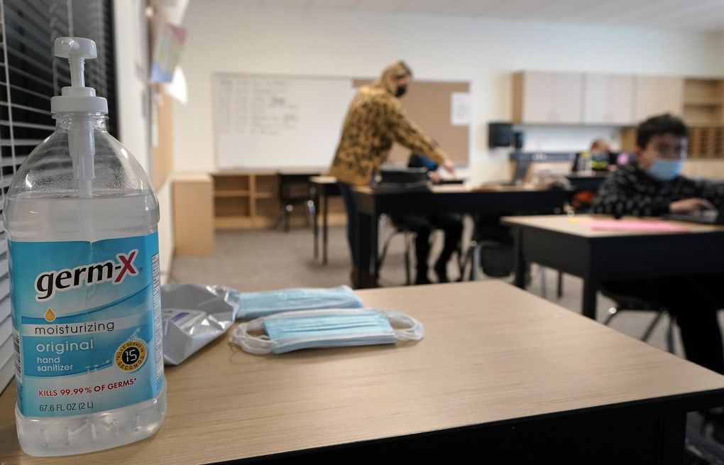 FILE – In this Feb. 2, 2021, file photo, hand sanitizer, wipes, and surgical masks rest on a desk in a fourth-grade classroom at Elk Ridge Elementary School in Buckley, Wash. Washington State authorities said Thursday, May 13, 2021, all schools in the state must provide full-time, in-person education for students for the 2021-22 school year and that students and staff will still be required to wear masks as a COVID-19 mitigation effort. (AP Photo/Ted S. Warren, File)