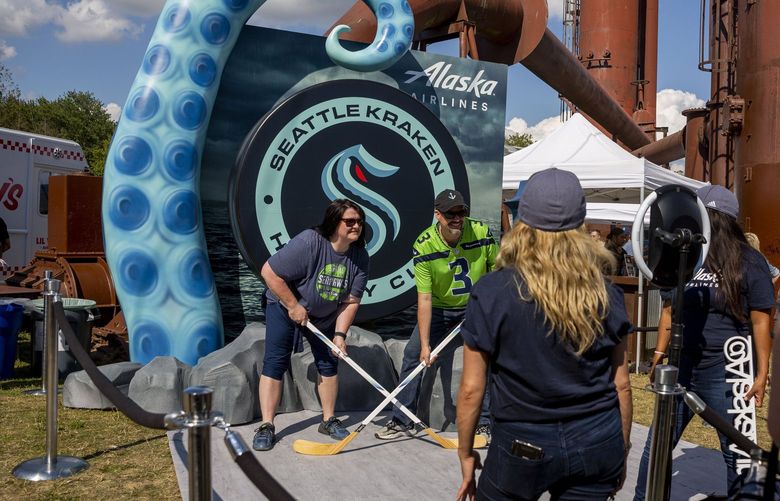 Brandy Freeman, 46, and Stuart Freeman, 46, of Lake Stevens take a photo with hockey sticks during the Seattle Kraken draft on Wednesday, July 21, 2021 at Gas Works Park in Seattle. (Sylvia Jarrus / The Seattle Times)