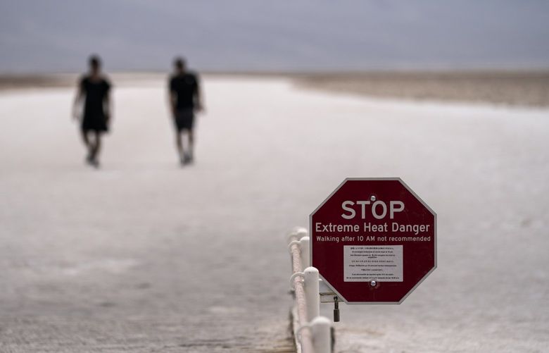A sign warns of extreme heat danger as people walk on salt flats in Badwater Basin, Sunday, July 11, 2021, in Death Valley National Park, Calif. Death Valley in southeastern California’s Mojave Desert reached 128 degrees Fahrenheit (53 Celsius) on Saturday, according to the National Weather Service’s reading at Furnace Creek. The shockingly high temperature was actually lower than the previous day, when the location reached 130 F (54 C). (AP Photo/John Locher) CAJL108 CAJL108