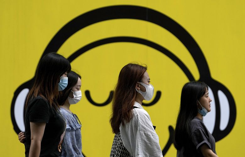Women wearing face masks to help curb the spread of the coronavirus walk by a smiley faces billboard during their lunch break in Beijing, Monday, July 19, 2021. (AP Photo/Andy Wong) 