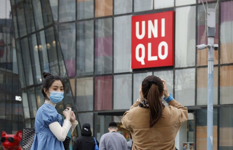 FILE – In this Monday, March 29, 2021 file photo, visitors to a shopping mall wearing masks stand before a Uniqlo store in Beijing. French prosecutors have on Friday, July 2 opened an investigation into alleged involvement in crimes against humanity based on accusations that global retailers, including Uniqlo and the makers of Skechers shoes and Zara clothes, rely on forced labor of minorities in China. (AP Photo/Ng Han Guan)