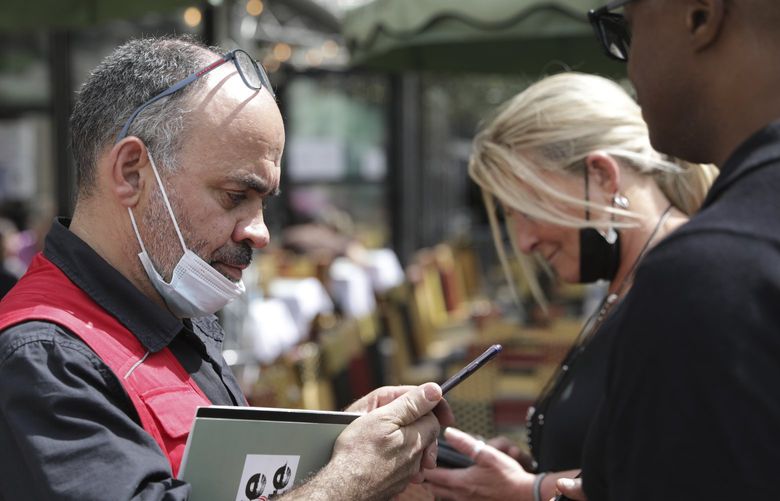 A waiter checks clients’ health passes at a restaurant in Paris, Monday Aug.9, 2021. People in France are now required to show a QR code proving they have a special virus pass to enjoy restaurants and cafes or travel across the country. The measure is part of a government plan to encourage more people to get the vaccine and to slow down a surge in infections, as the highly contagious delta variant now accounts for most cases in France.(AP Photo/Adrienne Surprenant) PAR119 PAR119