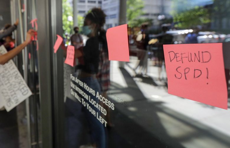 Protesters put adhesive notes on the doors of Seattle City Hall, Monday, July 13, 2020, following a news conference held by Mayor Jenny Durkan. Durkan and Police Chief Carmen Best were critical of a plan backed by several city council members that seeks to cut the police department’s budget by 50 percent. (AP Photo/Ted S. Warren) WATW117