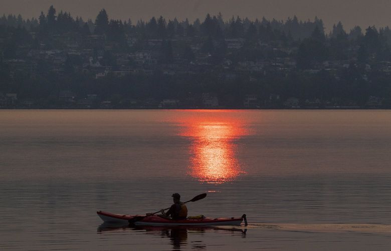 Friday, August 13, 2021.   A kayaker takes in a smokey morning sunrise on Lake Washington off Magnuson Park with a smokey Kirkland in the distance.    217928