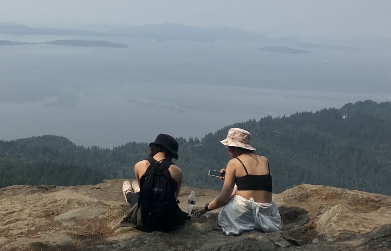 Hikers on the ledge at Oyster Dome, the rocky viewpoint on Mount Blanchard that affords panoramic views of the San Juan Islands and the Salish Sea.