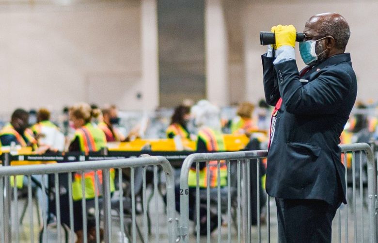 Bloomberg Best of the Year 2020: An official poll watcher uses binoculars as workers count ballots for the 2020 Presidential election at the Philadelphia Convention Center in Philadelphia, Pennsylvania, U.S., on Tuesday, Nov. 3, 2020. Photographer: Hannah Yoon/Bloomberg 775588261